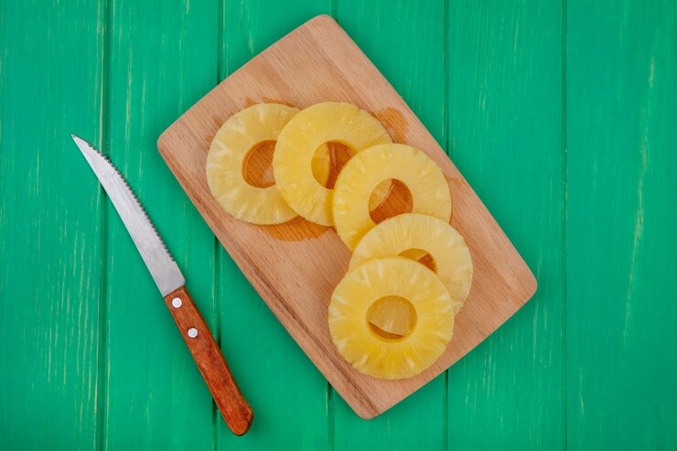 Foto gratuito vista superior de rodajas de piña en la tabla de cortar con un cuchillo en la superficie verde