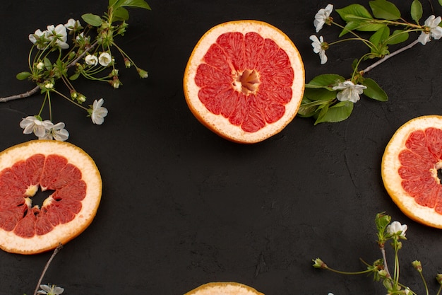 Vista superior rodajas de pomelo junto con flores blancas en el piso oscuro