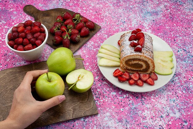 Vista superior rollo de pastel dentro de la placa con manzanas y fresas en el escritorio de color pastel galleta fruta dulce