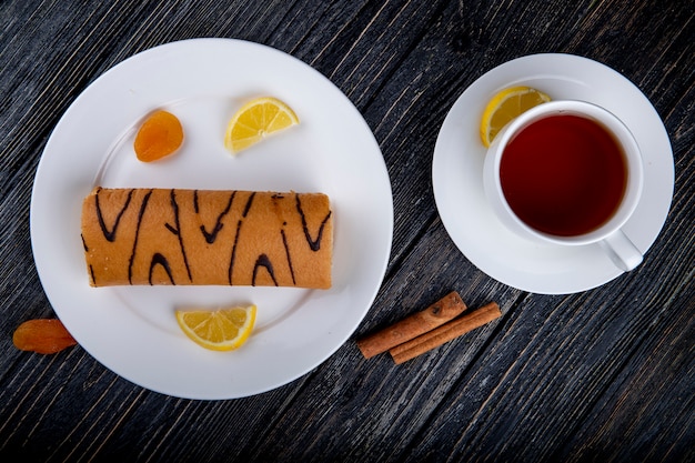 Foto gratuita vista superior del rollo suizo con mermelada de albaricoque en un plato blanco servido con una taza de té en rústico