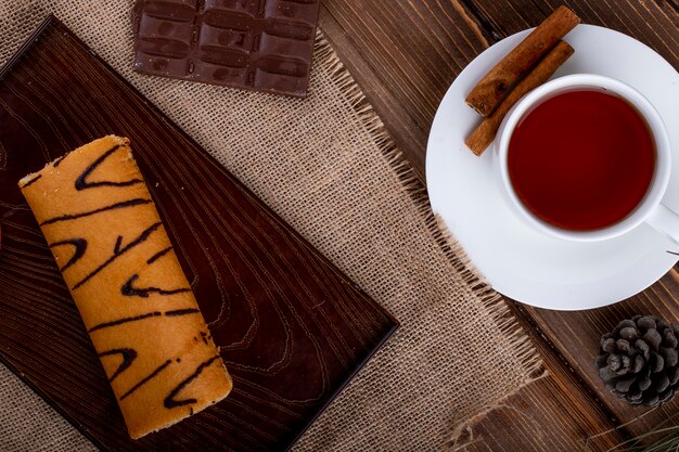 Vista superior del rollo suizo con mermelada de albaricoque en una tabla de madera servida con una taza de té en rústico