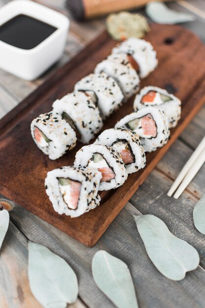 Vista superior del rollo de sushi en bandeja de madera con salsa de soja y palillos