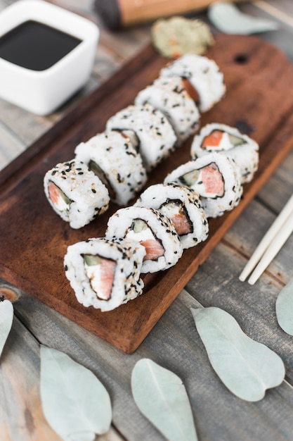 Vista superior del rollo de sushi en bandeja de madera con salsa de soja y palillos