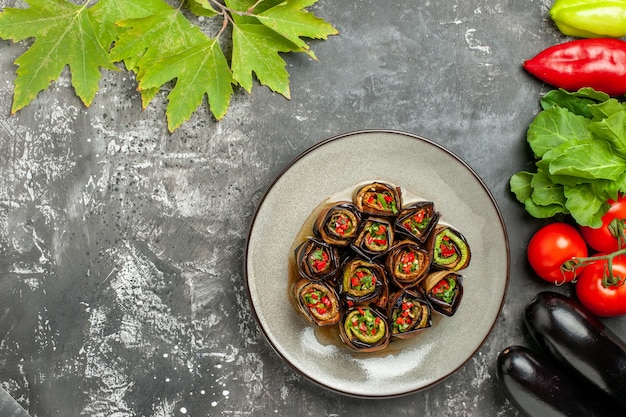 Vista superior rollos de berenjena rellena en plato blanco tomates pimientos berenjenas sobre fondo gris con espacio de copia