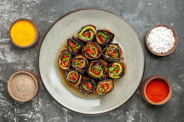 Vista superior rollos de berenjena rellenos pimiento picante en polvo cúrcuma sal marina pimienta negra en tazones pequeños sobre fondo gris