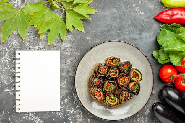 Foto gratuita vista superior rollos de berenjena rellenos en plato blanco tomates pimientos berenjenas un cuaderno sobre fondo gris plato