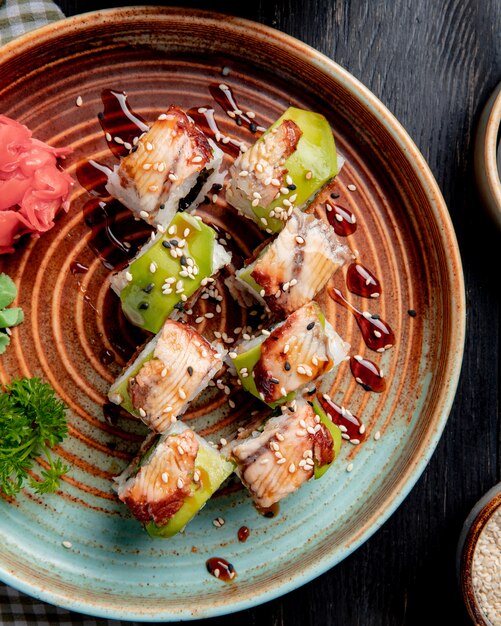 Vista superior de rollos de sushi con anguila, aguacate y pepino con jengibre y wasabi en un plato sobre madera