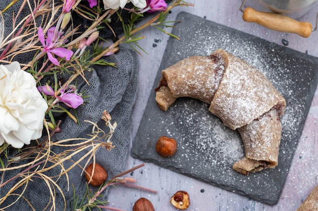 Vista superior de rollos veganos crudos, avellanas y flores blancas y rosadas sobre una superficie púrpura grunge