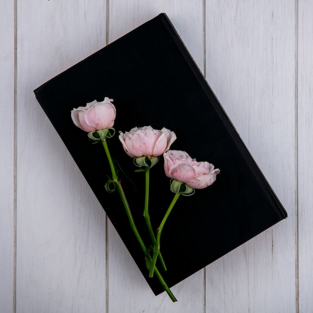 Vista superior de rosas de color rosa claro en un libro negro sobre una superficie gris