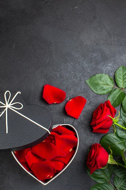 Vista superior de rosas rojas con caja llena de pétalos de rosa para el día de san valentín sobre fondo oscuro amor corazón pareja color pasión sentimiento