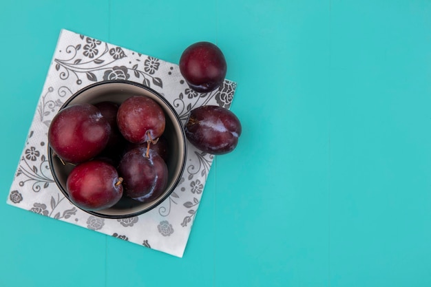 Vista superior del sabor king pluots en un tazón y en una servilleta sobre fondo azul con espacio de copia