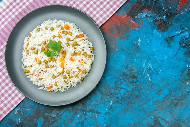 Vista superior de la sabrosa comida de arroz para la cena con zanahoria pisum en una toalla despojada de color púrpura en la mesa azul