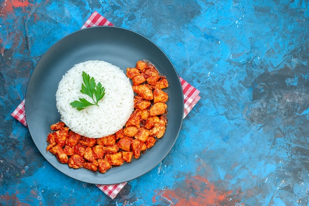 Foto gratuita vista superior de la sabrosa comida de arroz con pollo verde y tomate en una toalla despojada roja en la mesa azul