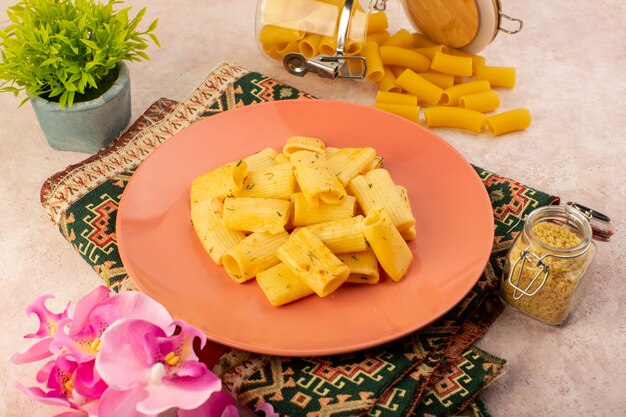 Una vista superior de la sabrosa comida de pasta italiana dentro de la placa rosa junto con la pasta cruda en la alfombra colorida y rosa