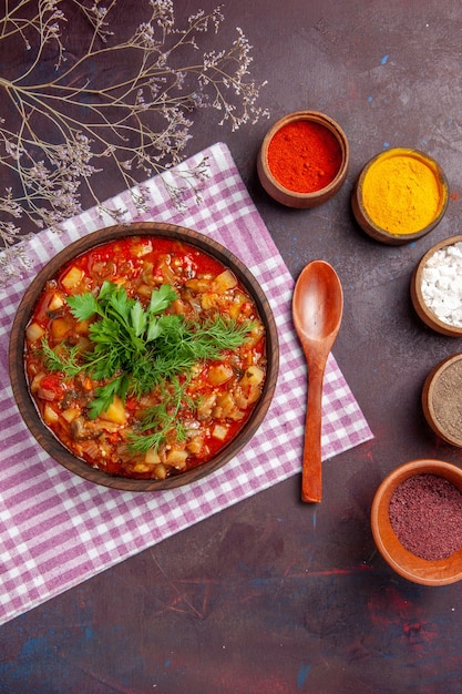 Vista superior sabrosa comida de salsa de verduras cocidas con diferentes condimentos en el plato de comida de salsa de superficie de color púrpura oscuro