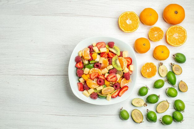 Vista superior sabrosa ensalada de frutas con feijoas frescas sobre fondo blanco.