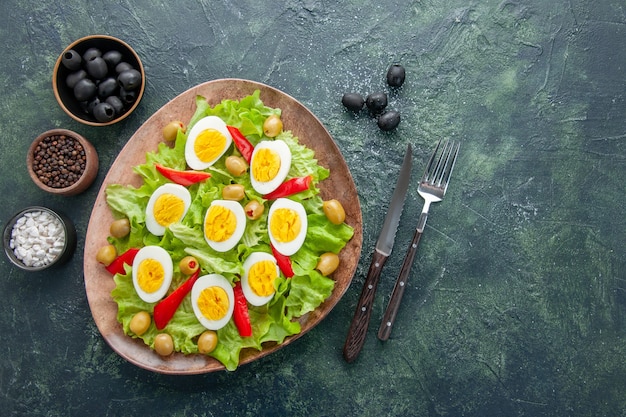 Vista superior sabrosa ensalada de huevo con ensalada de aceitunas verdes y condimentos sobre fondo oscuro