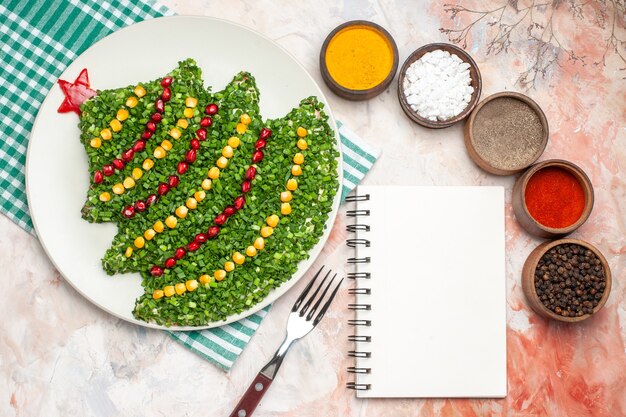 Vista superior sabrosa ensalada verde en forma de árbol de año nuevo con condimentos sobre fondo claro