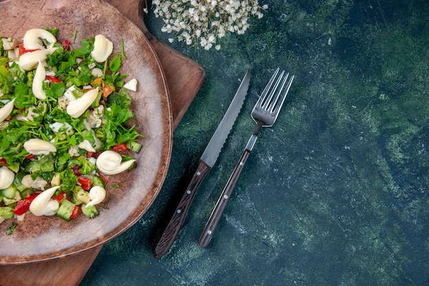 Foto gratuita vista superior sabrosa ensalada de verduras dentro de la placa con cubiertos sobre fondo azul oscuro cocina color de salud en forma cena cocina dieta almuerzo restaurante