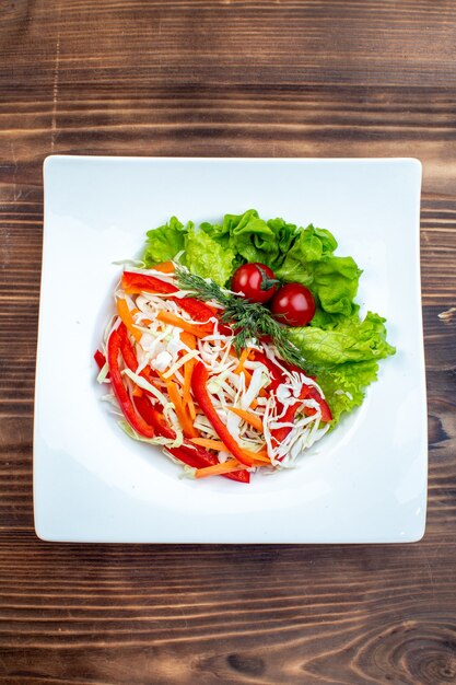 Vista superior sabrosa ensalada de verduras con ensalada verde y repollo dentro de la placa sobre superficie marrón