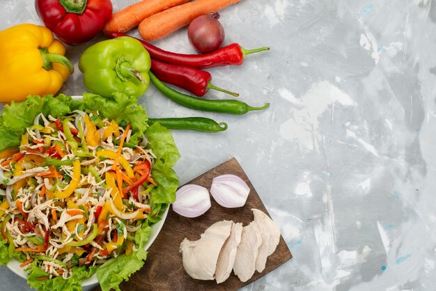 Vista superior sabrosa ensalada de verduras con verduras en rodajas y verduras frescas enteras y pechugas de pollo crudas en gris, comida de ensalada