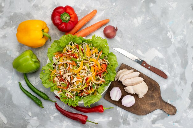 Vista superior sabrosa ensalada de verduras con verduras en rodajas y verduras frescas enteras y pechugas de pollo crudas en gris, comida de ensalada