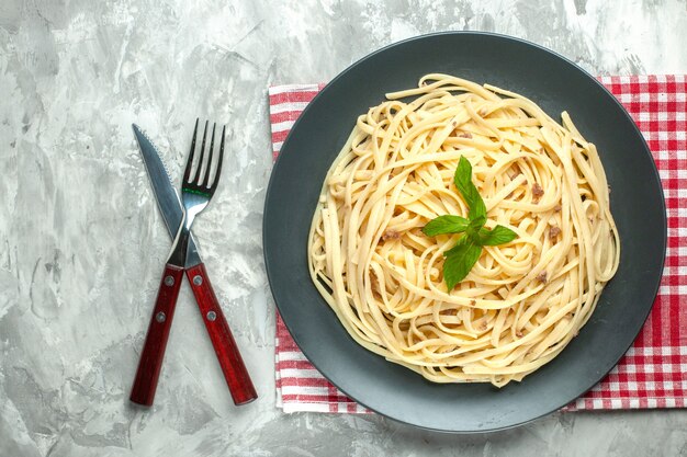 Vista superior de la sabrosa pasta italiana con cubiertos sobre fondo blanco.