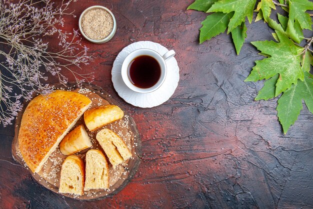 Vista superior de la sabrosa pastelería dulce cortada en trozos con una taza de té sobre una superficie oscura