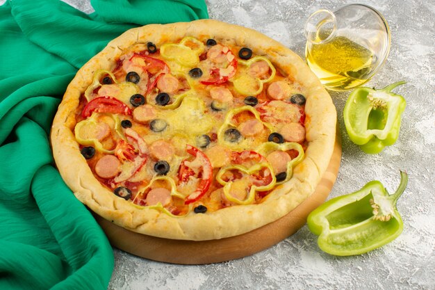 Vista superior de sabrosa pizza con queso con aceitunas negras, salchichas y tomates rojos junto con pimientos y aceite en el escritorio gris, comida rápida, masa italiana, hornear