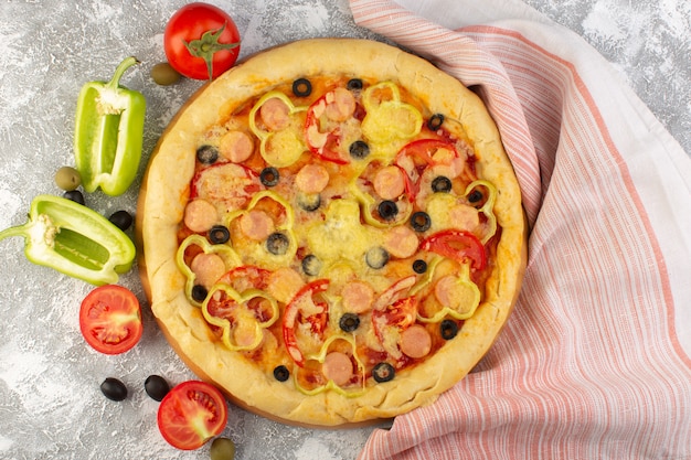 Vista superior de la sabrosa pizza con queso con aceitunas negras, salchichas y tomates rojos sobre el fondo gris, comida rápida, masa italiana, hornear