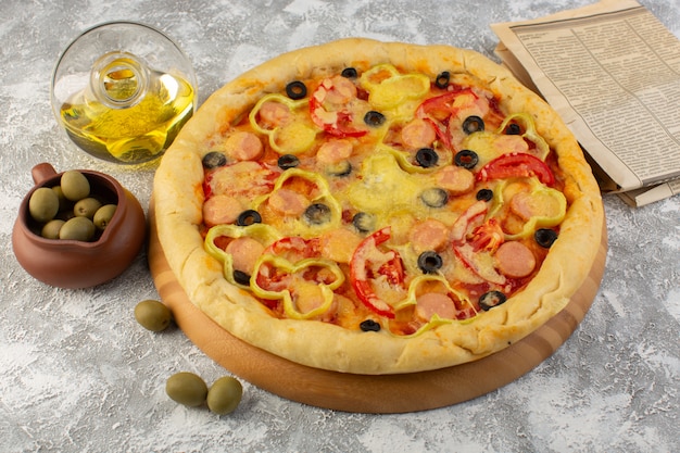 Vista superior sabrosa pizza con queso con salchichas de aceitunas negras y tomates rojos junto con aceite en el escritorio gris horneado de masa italiana de comida rápida