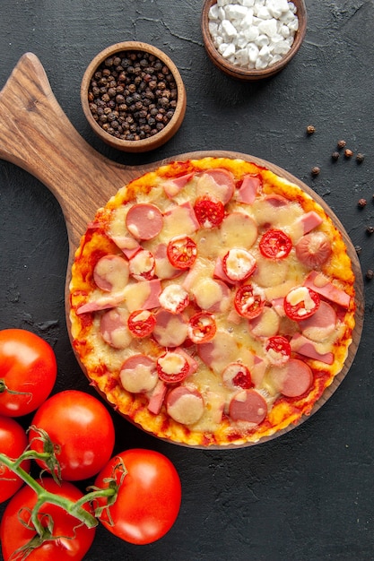 Vista superior de la sabrosa pizza de queso con salchichas y tomates en la mesa oscura