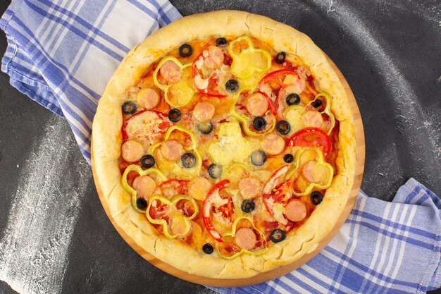 Vista superior de la sabrosa pizza con queso con tomates rojos, aceitunas negras y salchichas en el fondo oscuro con una toalla, comida de comida rápida, masa italiana