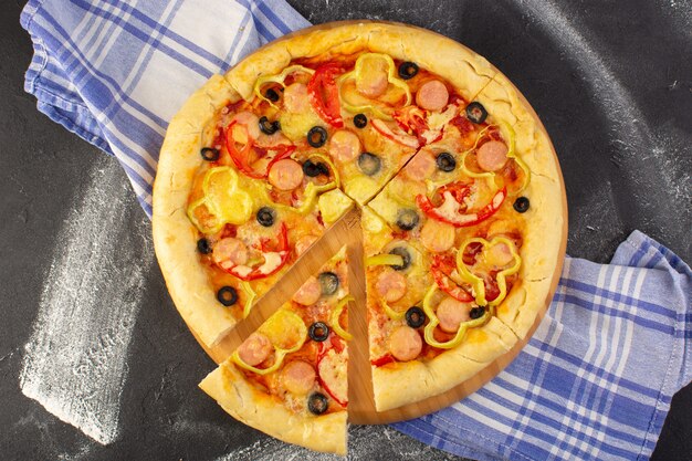 Vista superior de la sabrosa pizza con queso con tomates rojos, aceitunas negras y salchichas en el fondo oscuro con una toalla de masa italiana de comida rápida