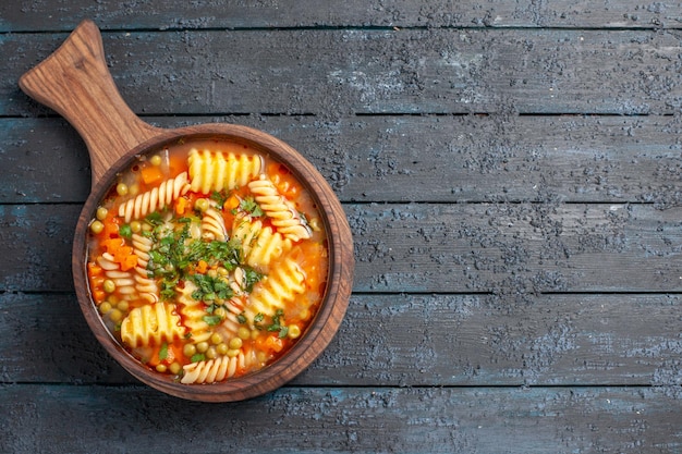 Vista superior de la sabrosa sopa de pasta de pasta italiana en espiral con verduras en el plato de cocina de pasta italiana de color azul oscuro sopa de escritorio