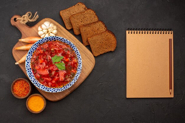 Vista superior sabrosa sopa de remolacha ucraniana borsch con panes de pan oscuro en el espacio oscuro