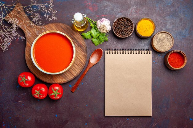 Vista superior de la sabrosa sopa de tomate con condimentos y tomates frescos en la oscuridad