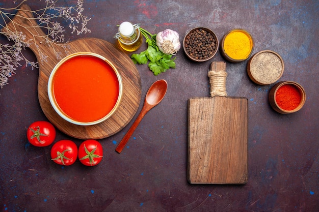 Vista superior de la sabrosa sopa de tomate con condimentos y tomates frescos en la oscuridad