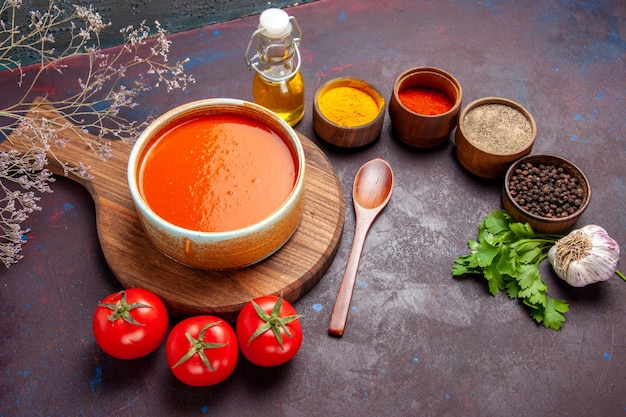 Vista superior de la sabrosa sopa de tomate con tomates frescos y condimentos en el espacio oscuro