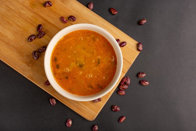 Vista superior de la sabrosa sopa de verduras dentro de la placa junto con frijoles crudos en la superficie oscura