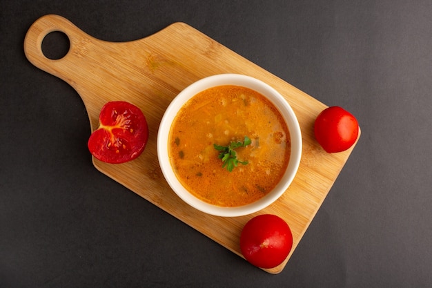 Vista superior de la sabrosa sopa de verduras dentro de la placa junto con los tomates en la superficie oscura