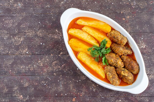 Vista superior sabrosas chuletas de carne cocidas junto con patatas y salsa dentro de la placa en el fondo de madera marrón carne plato de patatas cena