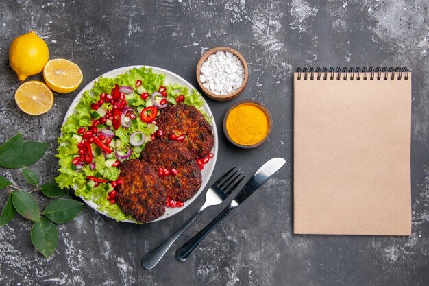 Vista superior sabrosas chuletas de carne con ensalada y condimentos en un plato de comida con foto de piso gris