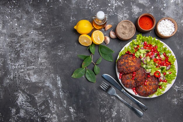 Vista superior sabrosas chuletas de carne con ensalada de verduras en el plato de comida de la foto del escritorio gris