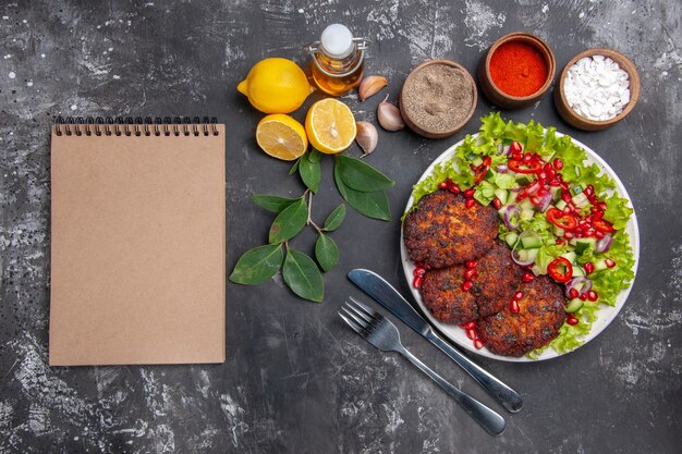 Vista superior sabrosas chuletas de carne con ensalada de verduras en el plato de comida de foto de fondo gris