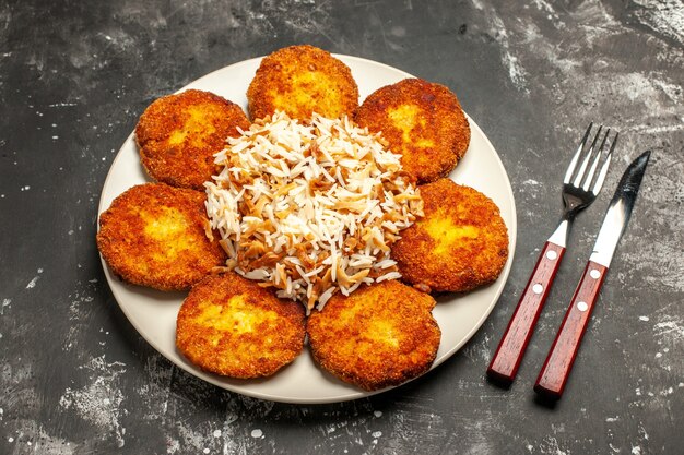 Vista superior sabrosas chuletas fritas con arroz cocido en la superficie oscura plato comida foto carne