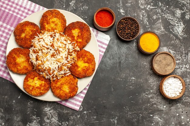 Vista superior sabrosas chuletas fritas con arroz y condimentos en rissole de carne de superficie oscura