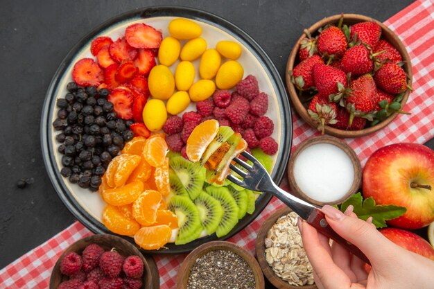 Vista superior de sabrosas frutas en rodajas con bayas frescas y frutas sobre fondo oscuro