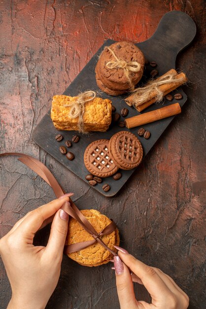 Vista superior sabrosas galletas atadas con cuerda, canela, galletas, galletas de mesa de madera para servir, en manos femeninas en la mesa oscura