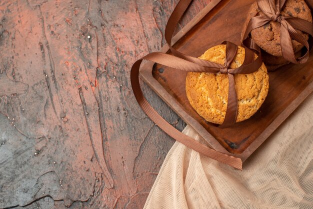 Vista superior sabrosas galletas atadas con una cuerda en el tablero de madera en el espacio libre de la mesa de color rojo oscuro